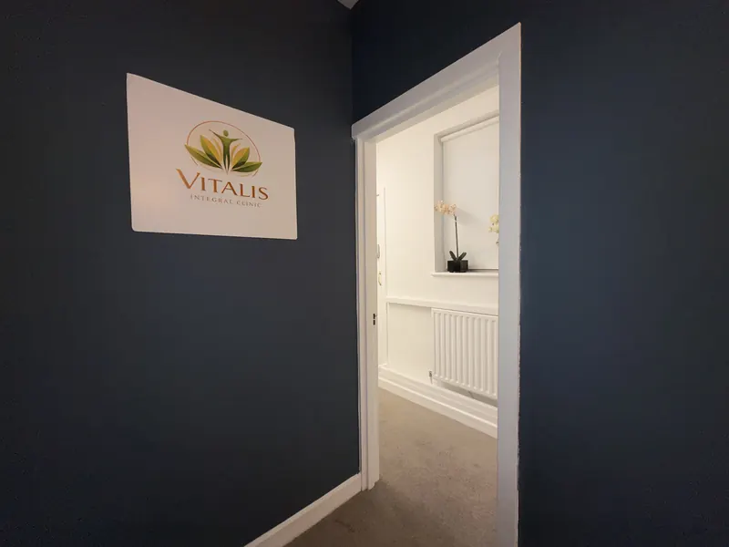 Cartel de Vitalis Integral Clinic en el pasillo, junto a la puerta abierta de una sala luminosa